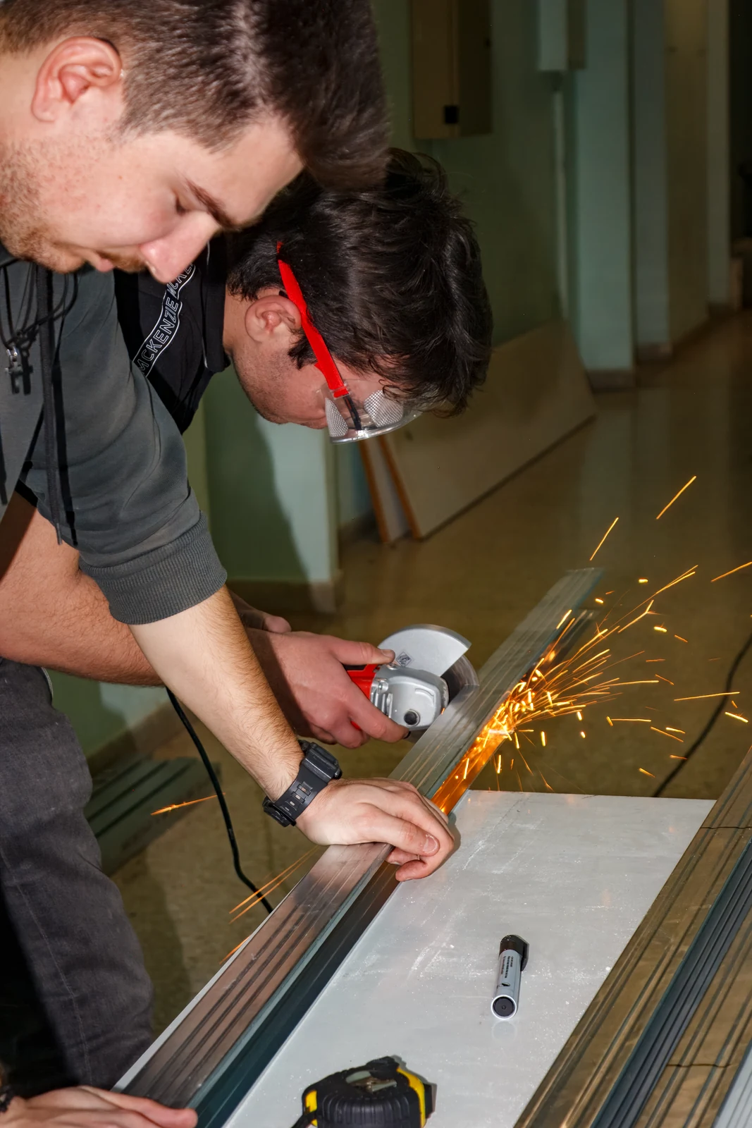 Team members cut a metal section with an angle grinder in the workshop